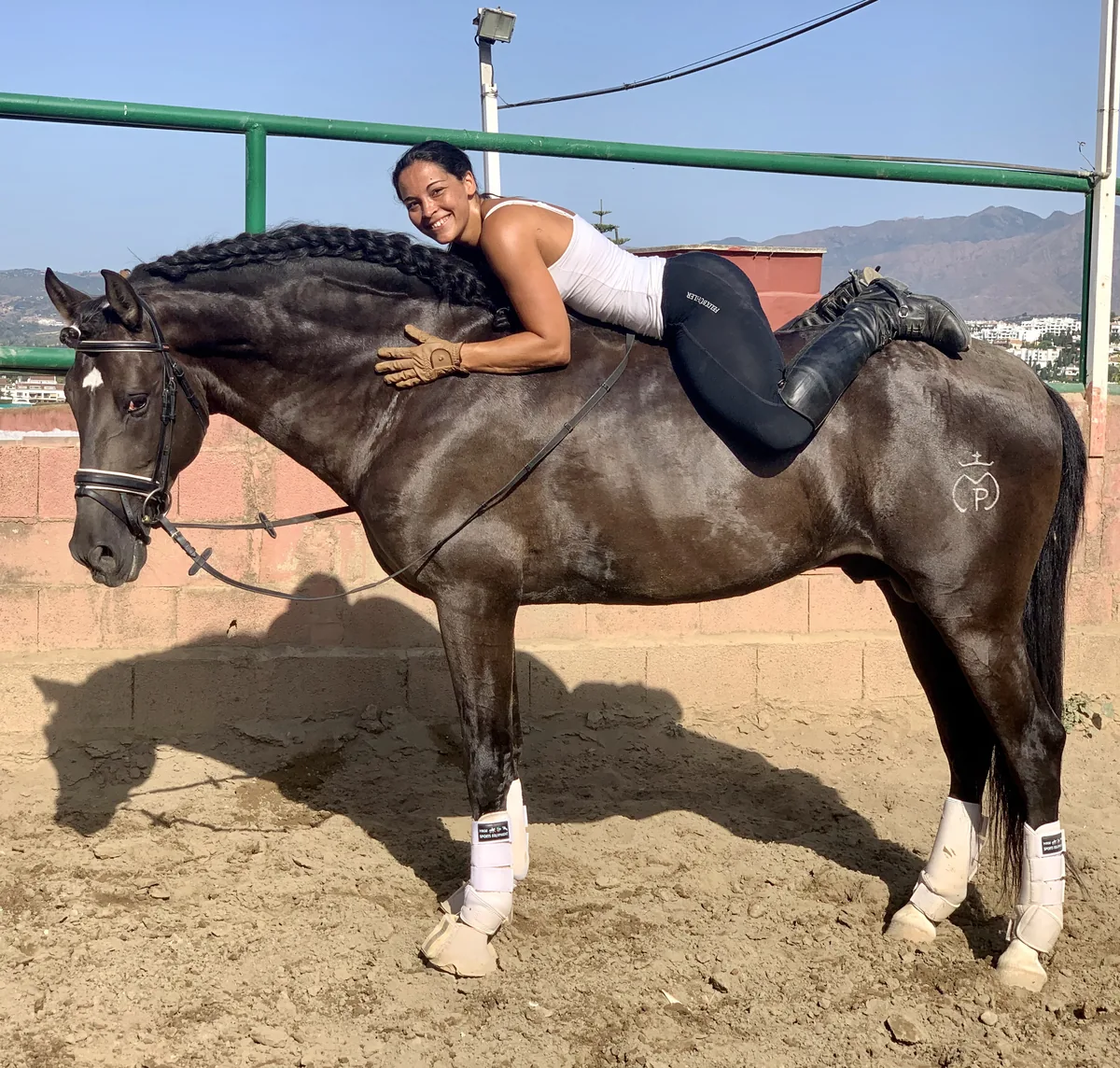 Angelina Zanker lying relaxed on the back of a black stallion with a plaited mane
